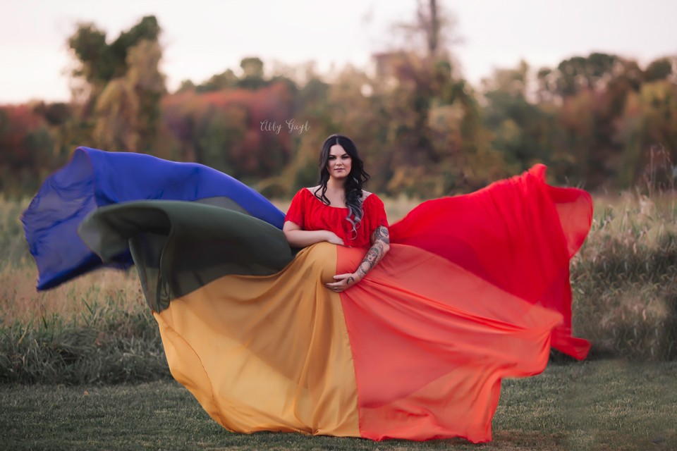 Pregnant woman posing outdoors in brightly colored flying maternity gown