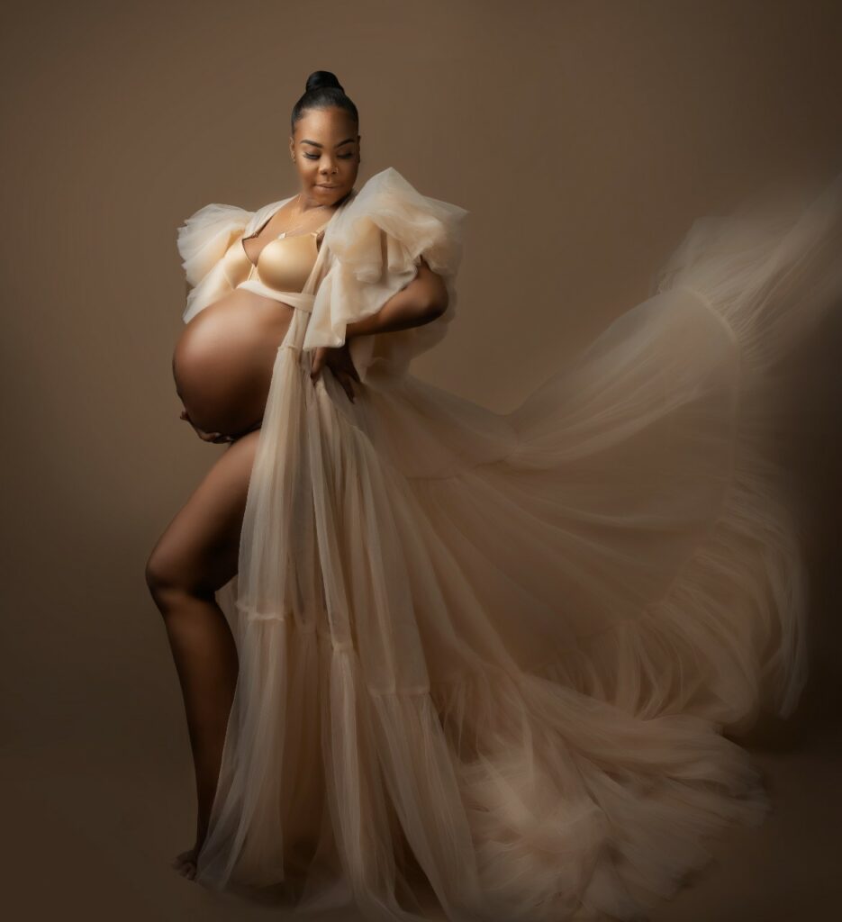 Pregnant woman posing in ivory flowing open belly maternity gown