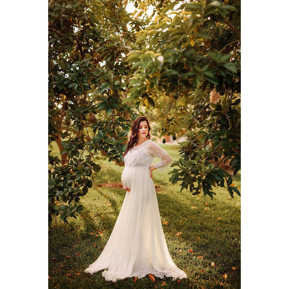 Pregnant woman posing outside in white flowing maternity gown