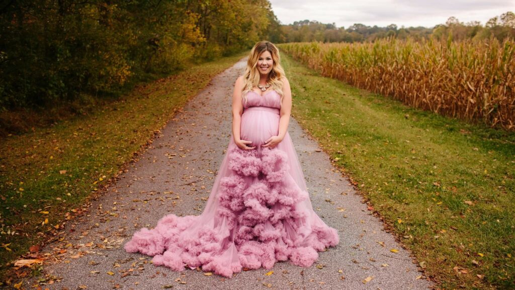 Pregnant woman standing on country lane in a pink ruffled maternity gown