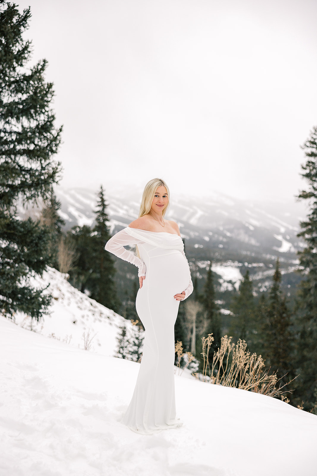 pregnant woman in a white maternity gown on a mountain in the snow in Breckenridge